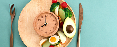 Maaltijd met groenten, avocado en ei met een klok als symbool voor eetmomenten Maaltijd met groenten, avocado en ei met een klok als symbool voor eetmomenten