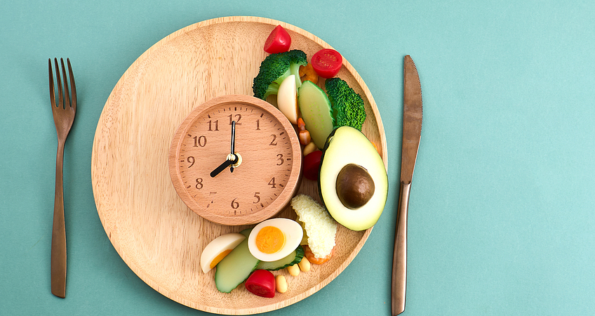 Maaltijd met groenten, avocado en ei met een klok als symbool voor eetmomenten Maaltijd met groenten, avocado en ei met een klok als symbool voor eetmomenten